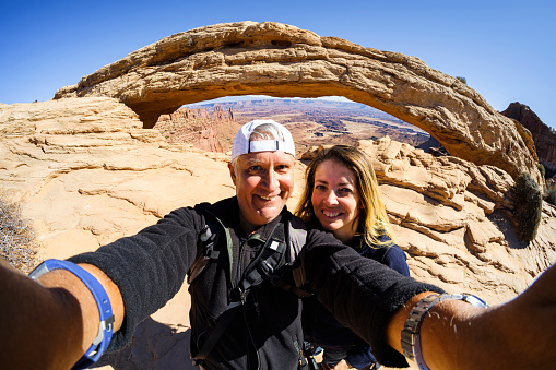 Happy couple enjoying the natural beauty of the famous Mesa Arch in Canyonlands National Park.