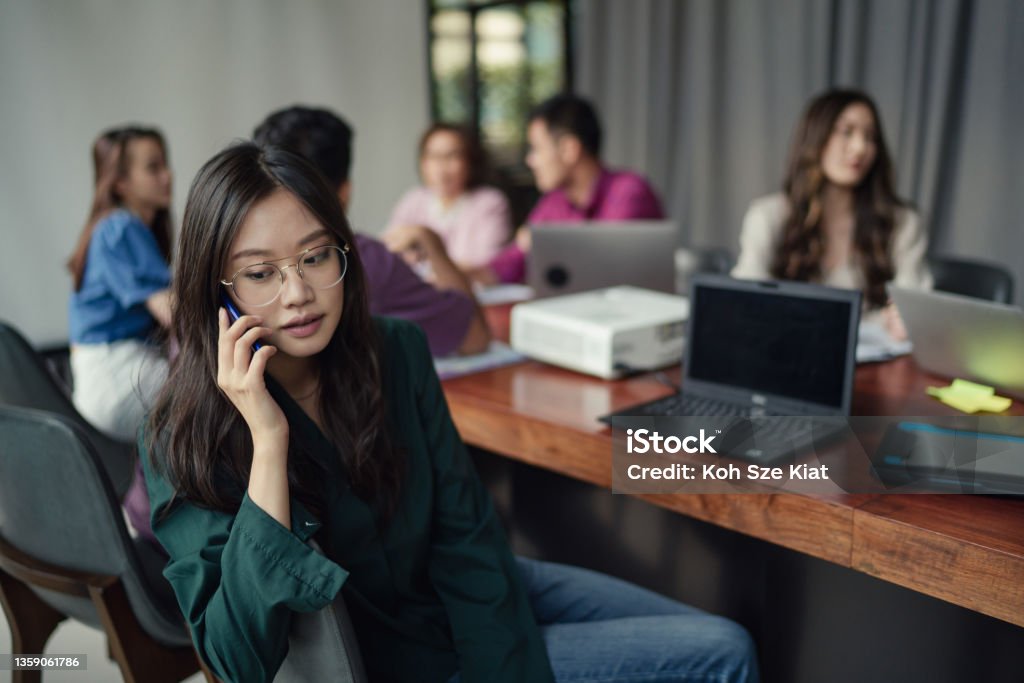 Woman turns away from a meeting to answer a call Whispering Stock Photo