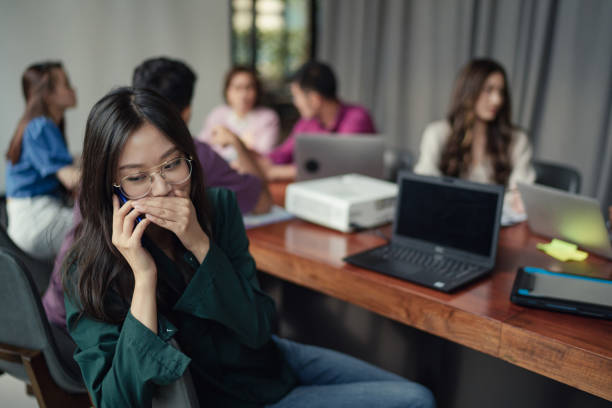 会議中に電話でささやくアジアの女性 - inconvenience meeting business distracted ストックフォトと画像