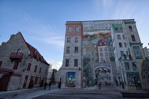 Quebec City, Quebec, Canada - November 22, 2021:  Tourists walking by the Mural in Petit Champlain district. The area and the whole of the walled city of Old Quebec is designated as a UNESCO World Heritage Site.