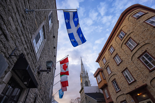 Quebec City, Quebec, Canada- November 23, 2021: Old town Quebec City street scene in early morning. Quebec flag and Canadian flag and other countries' flags on the exterior wall of a hotel.