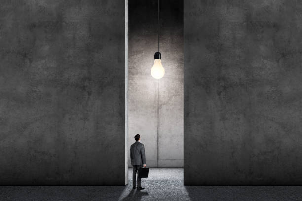istock Man Standing In Large Room Illuminated By Single Light Bulb 1359071230