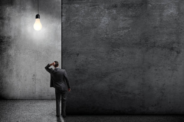istock Man Standing In Large Room Illuminated By Single Light Bulb 1359071233