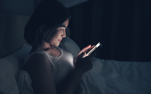 Woman sending messages on cellphone and lying on bed.