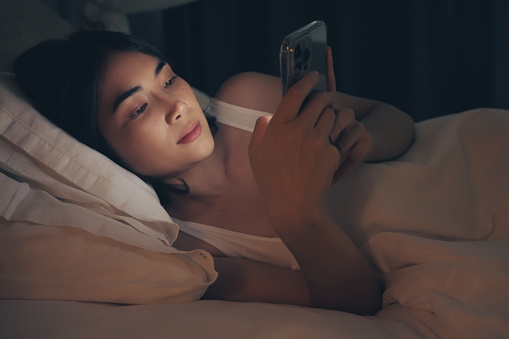 Woman are using phone on the bed before she sleeping at night.