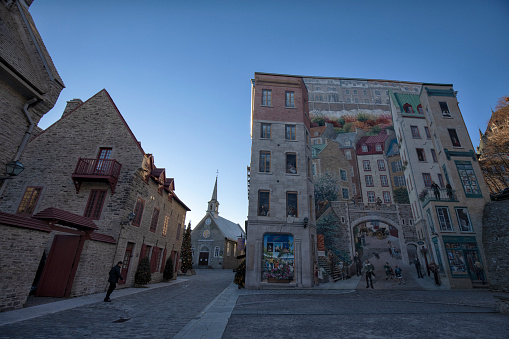 Quebec City, Quebec, Canada - November 24, 2021:  Tourist walking by the Mural in Petit Champlain district. The area and the whole of the walled city of Old Quebec is designated as a UNESCO World Heritage Site.