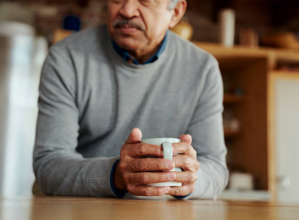 feche acima das mãos de pensativo aposentado homem biracial idoso apoiado em balcão de cozinha moderno, segurando café da manhã em suas mãos - senior adult human face male action - fotografias e filmes do acervo