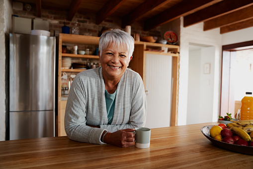 Portrait of biracial elderly female leaning on kitchen counter smiling at camera.