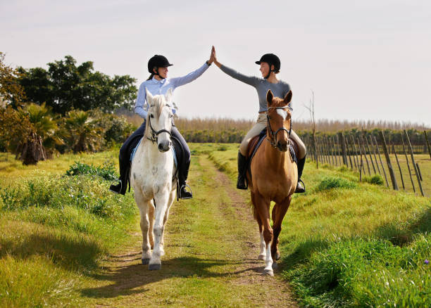 plan complet de deux jeunes femmes en train de faire du fiving alors qu’elles montaient à cheval sur le ranch - bride women standing beauty in nature photos et images de collection
