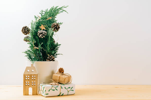 istock Creative natural miniature Christmas tree in pot on wooden table with gift boxes and white background. Xmas greeting card with copy space. Happy New Year 1359093432