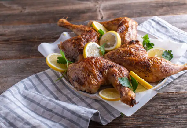 Homemade fresh cooked roasted or grilled chicken legs. Served hot on a plate with sliced lemon and parley isolated on wooden table.