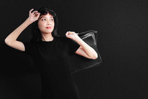 Asian woman with sunglasses carrying a shopping bag with a black background. Black Friday concept