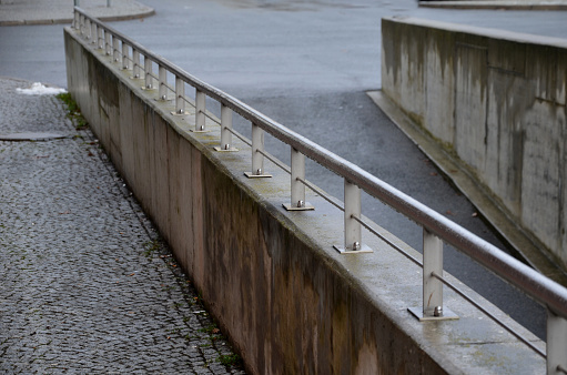 concrete entrance to the underground garage or tunnel. the railing around it is formed by a wall and a stainless steel bar as a handrail in the pedestrian zone