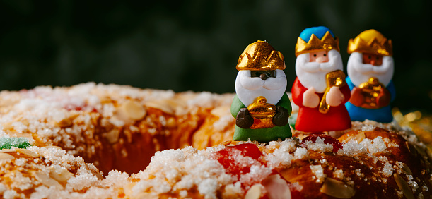 the three wise men, melchior, caspar and balthazar, on top of a roscon de reyes, the spanish three kings cake eaten on epiphany day, in a panoramic format to use as web banner or header