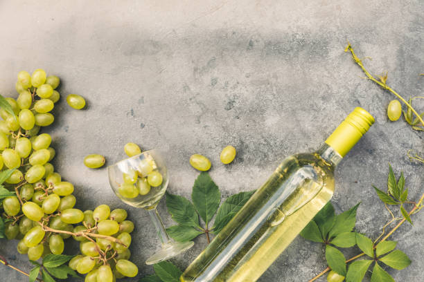 top view of bottle white wine, green vine, wineglass and ripe grape on vintage gray stone table background. wine shop wine bar winery or wine tasting concept - wine glass white wine wineglass imagens e fotografias de stock