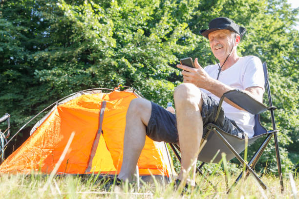 istock Elderly camper sitting by a tent and text messaging 1359103324