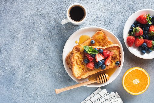 Sweet french toast with syrup and berries and cup of coffee on concrete table background, top view, copy space. Continental breakfast