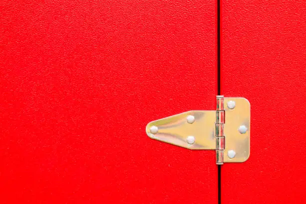 Construction details, silver objects concept. Closeup of metal steel hinge on red door