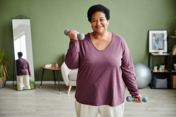 Smiling Senior Woman Working Out at Home Waist up portrait of black senior woman holding dumbbells and enjoying workout at home smiling happily, copy space home workout stock pictures, royalty-free photos & images