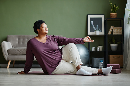 Full length portrait of active senior woman doing yoga at home and meditating, copy space