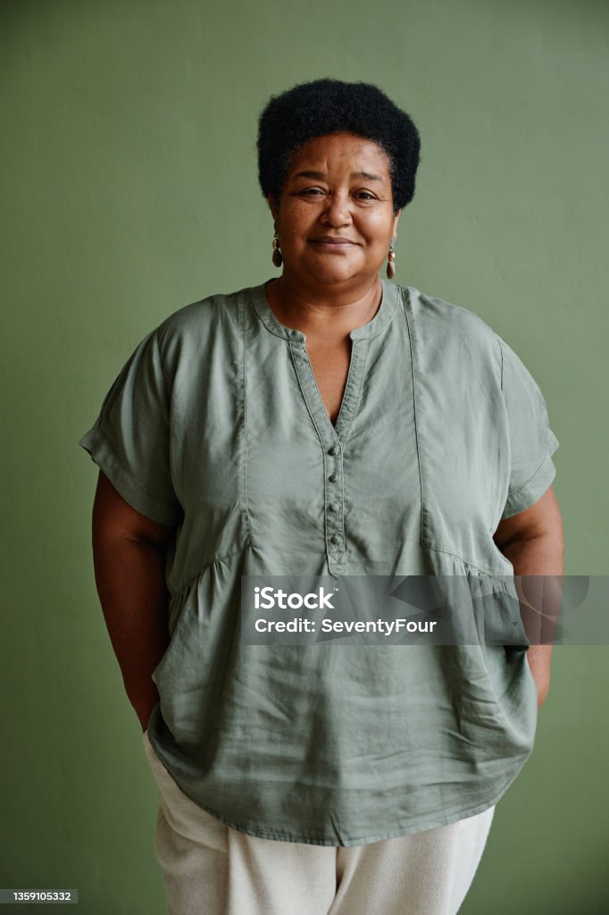 Portrait of Black Senior Woman on Green Vertical portrait of black senior woman smiling at camera while standing against green background Women Stock Photo