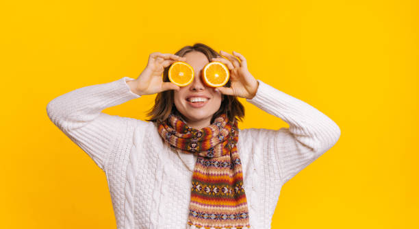 Young female in casual outfit looking at camera and covering eyes with sliced orange stock photo