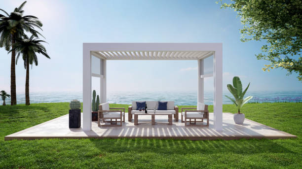 3D illustration of garden patio with white pergola next to sea. 3D render of luxury deck on grass plain with white bio climatic pergola. Cozy sofa set with coffee table, palm trees and relaxing sea view. wooden porch stock pictures, royalty-free photos & images