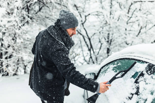istock Young man cleans a car windshield from snow with a brush. 1359110166