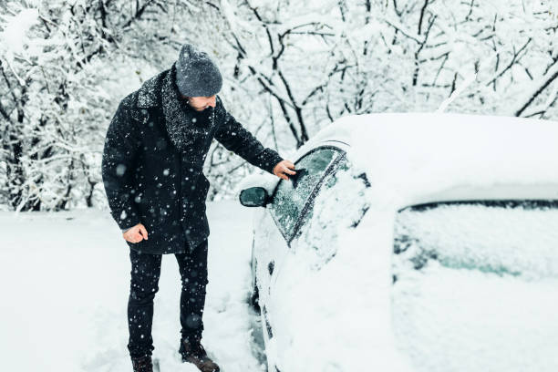istock Young man cleans a car windshield from snow with a brush. 1359110169