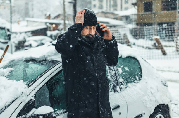 istock Mature man in snow with broken down car.  man calling the car service standing on the broken car in the winter 1359110313
