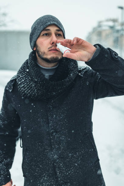 istock Cold and flu. Young sick man uses a nose spray at street . 1359110891