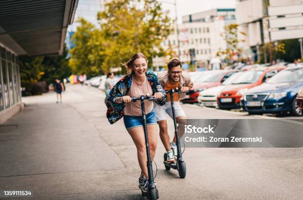 Young Couple On Vacation Having Fun Driving Electric Scooter Through The City Stock Photo - Download Image Now