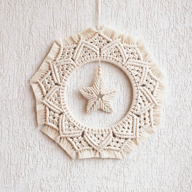 Christmas decor. Macrame wreath for Christmas and the new year on a white decorative plaster wall. Natural cotton thread, linen tape. Eco decor for home. Copy space stock photo