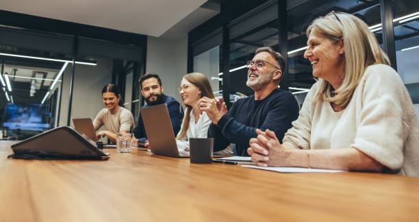 Cheerful business professionals laughing during a briefing Cheerful business professionals laughing during a briefing. Group of happy businesspeople enjoying working together in a modern workplace. Team of diverse colleagues having a meeting in a boardroom. business conference photos stock pictures, royalty-free photos & images