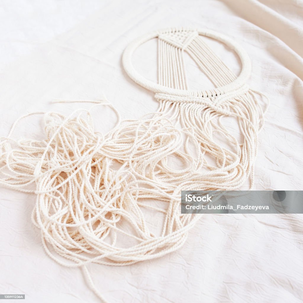 Handmade cotton macrame Dream catcher during fabrication. Traditional amulet for protecting sleep. Close up. Macrame lace on textile background. Shabby chic. Woman hobby. Copy space. Craft Stock Photo