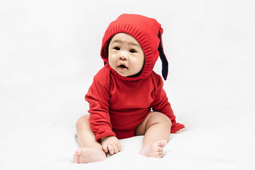 Happy infant baby boy toddler in red bodysuit and knitted hat with rabbit ears.Concept holiday Christmas, happy new year, infants, childhood.