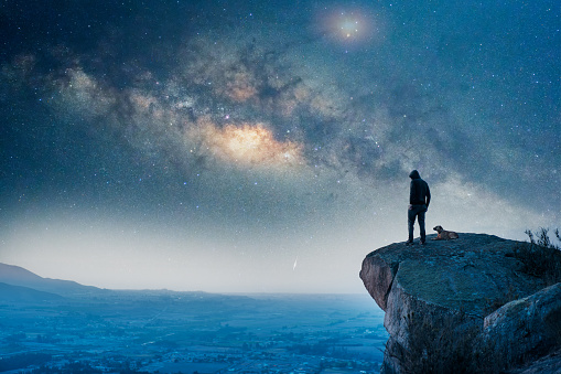 man standing on the top of the mountain, back view, with his dog and Milky Way over the valley