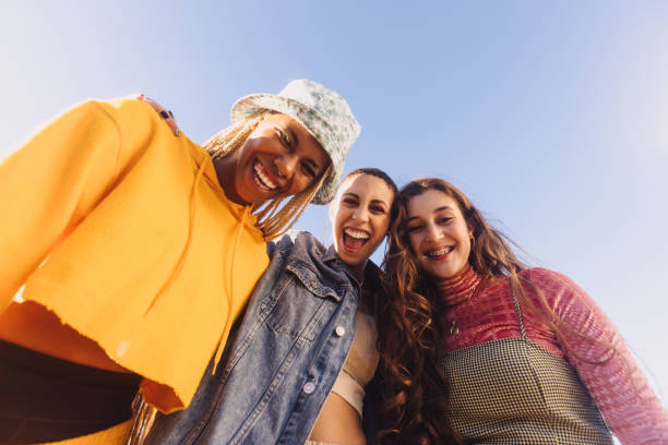 vista ad angolo basso di tre amici che sorridono allegramente - inquadratura dal basso foto e immagini stock