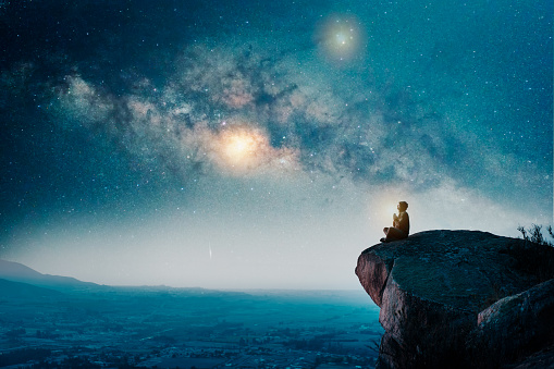 person sitting on the top of the mountain meditating or contemplating the starry night with Milky Way background