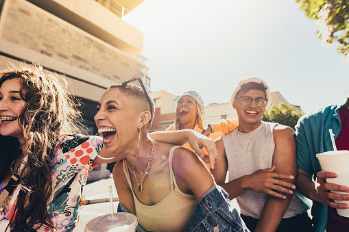 Enjoying friendship and youth. Group of generation z friends laughing cheerfully while walking together in the summer sun. Happy young friends having fun while hanging out together outdoors.