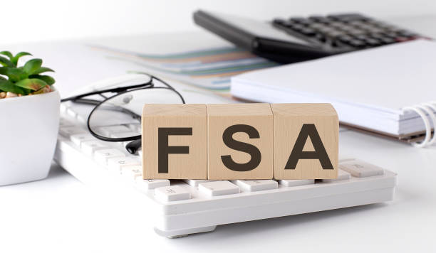 FSA written on a wooden cube on keyboard with office tools stock photo