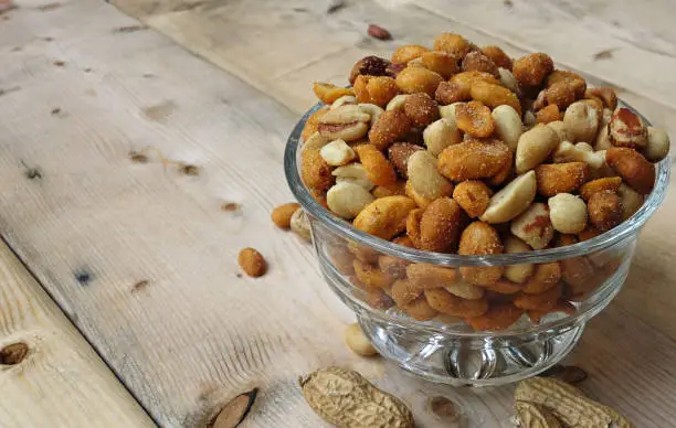 Close up view of mixed peanuts in a glass bowl, defocused food background photo.