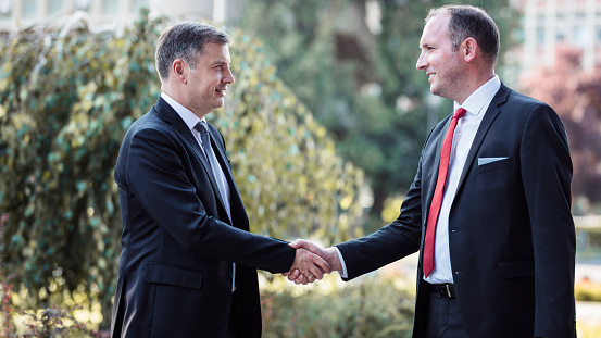 Business people supporting each other, shaking hands when running into one another outdoors and smiling