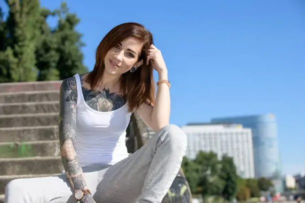 A beautiful young tattooed woman is walking in the city and enjoys the warm summer.