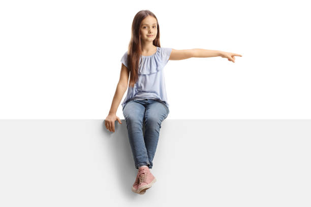 istock Girl sitting on a blank panel and pointing to the side 1359121252