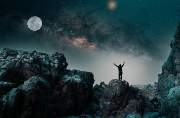 istock man standing on the mountain, back view, with raised hands with Milky Way and Moon background 1359125146