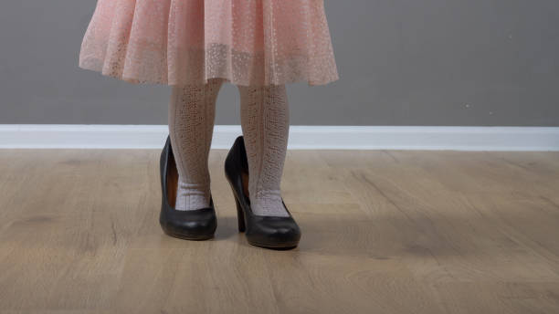 Cute baby girl 2 years old caucasian walks in black mom's big heels in pink prom dress stock photo