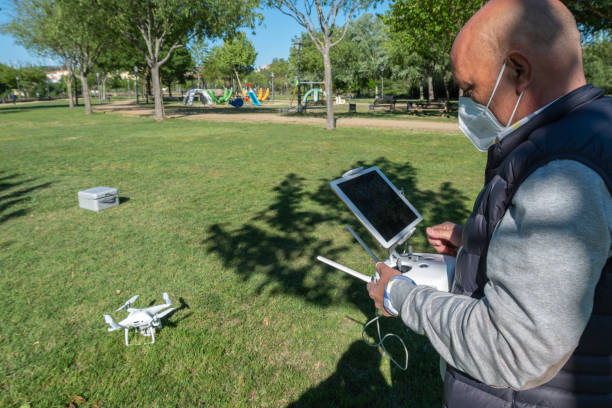 un uomo adulto che indossa una maschera contro il covid-19 mantiene il controllo pilotando un drone - pilotando foto e immagini stock