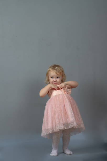 Cute baby girl 2 years old caucasian dancing in pink prom dress on a gray background in the studio Cute baby girl 2 years old caucasian dancing in pink prom dress on a gray background in the studio. pink gown stock pictures, royalty-free photos & images