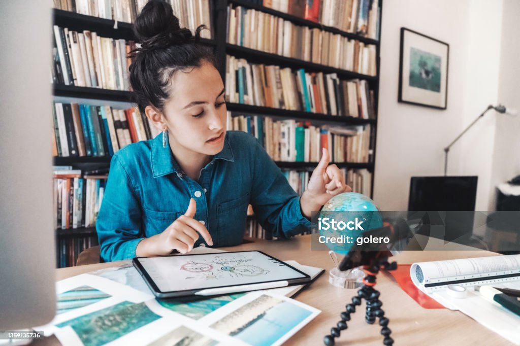teenage girl preparing presentaion for climate change issues on digital tablet and globe teenage girl sitting at desk in front of book shelf and looking at globe and digital tablet Student Stock Photo